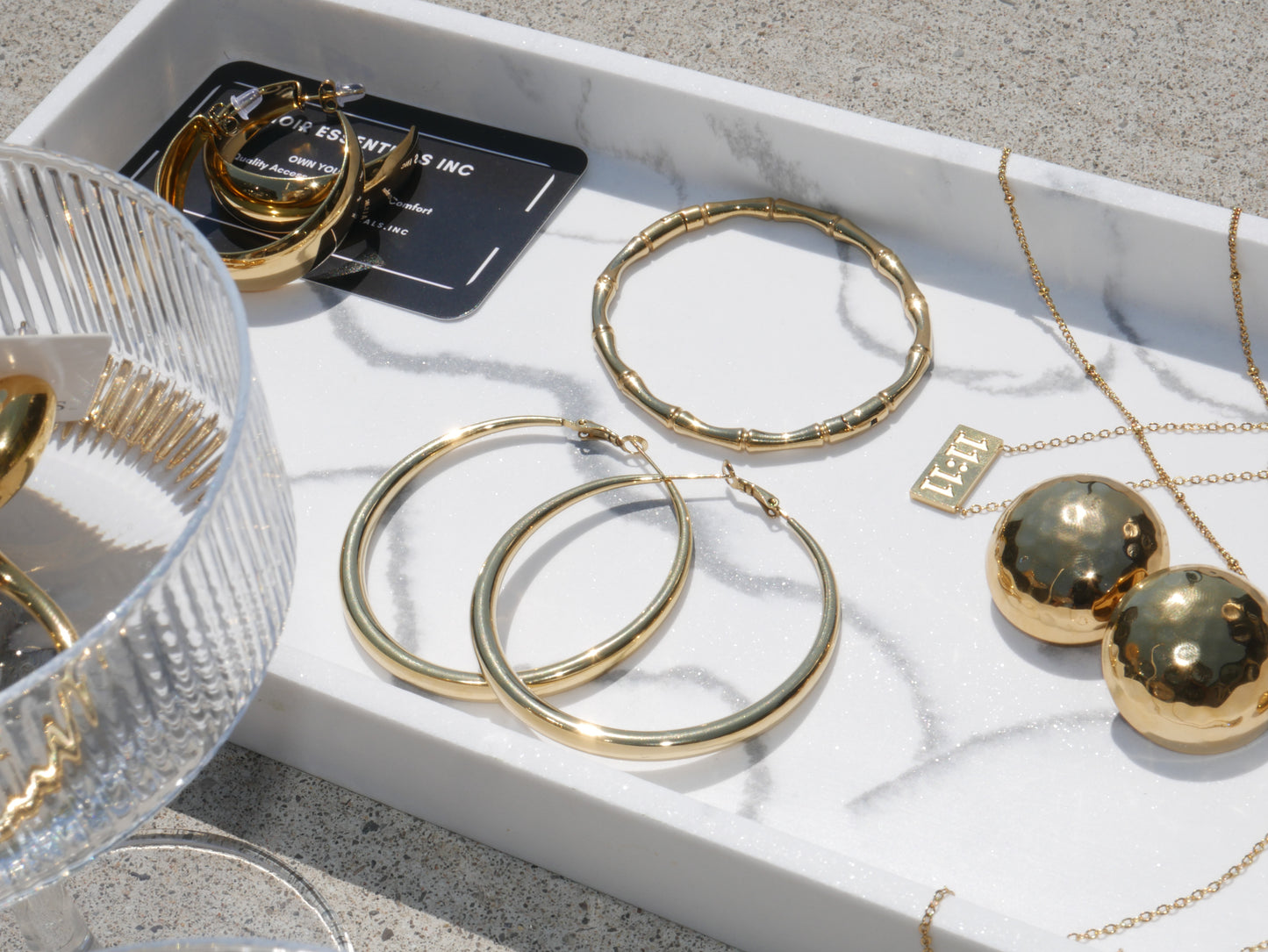 Gold hoop earrings and necklaces on a white tray with a clear glass bowl.